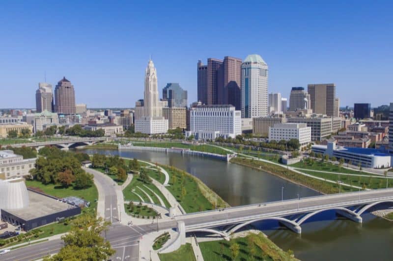 Columbus Ohio Aerial view of a downtown skyline with tall buildings, a curving river, green park and bridges nearby
