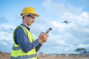 Surveyor operating aerial mapping equipment while a drone captures site data for land development and terrain analysis